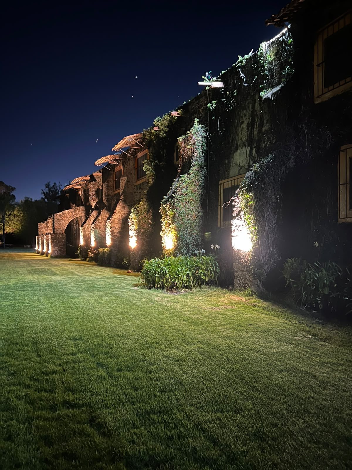 Jardín y corredor de arcos iluminados de noche en Hacienda Dolores, Querétaro